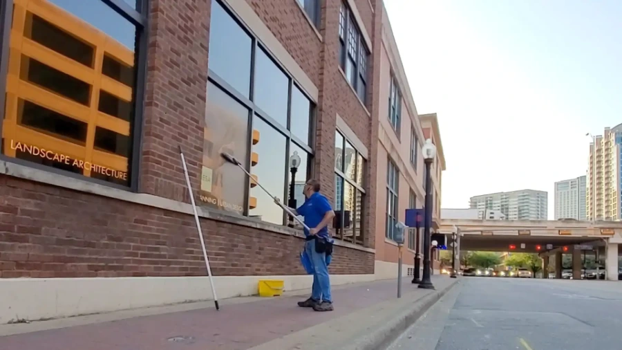 Technician cleaning street-level office windows outside a commercial building