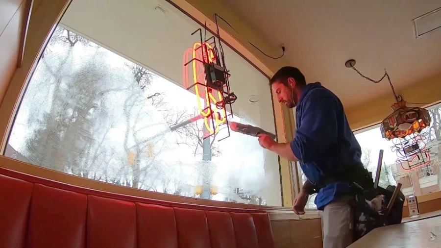 Technician cleaning the interior of a restaurant's front window