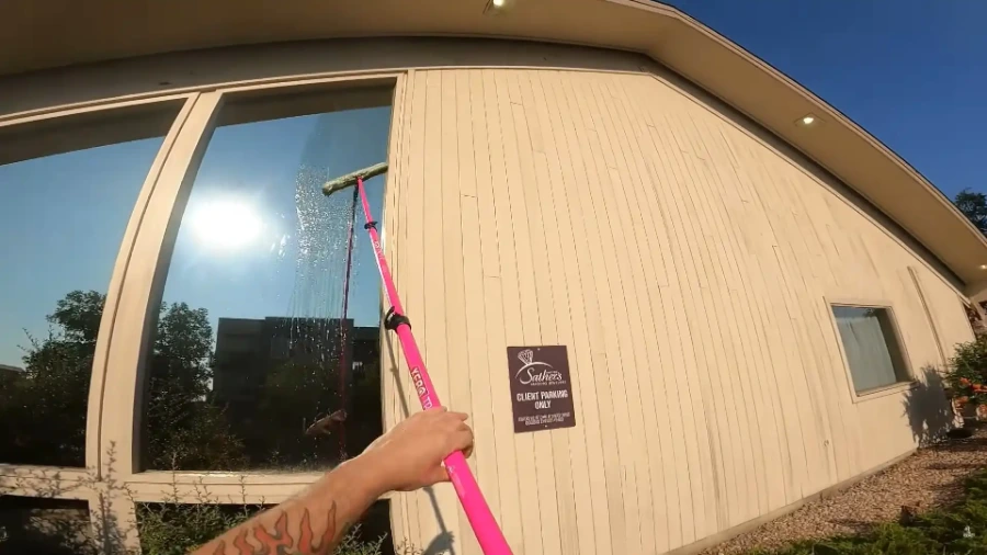 Technician using a pole squeegee to clean a large window on a commercial building, with a wall sign visible