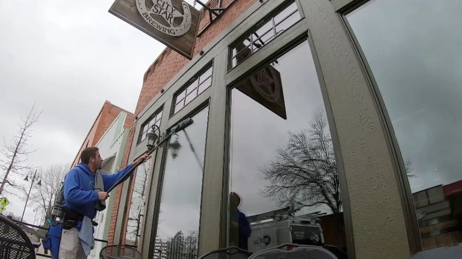 Technician using a water-fed pole to clean storefront windows outside a San Clemente brewery